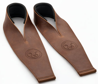 Two brown leather weightlifting straps with black neoprene wrist support on a white background